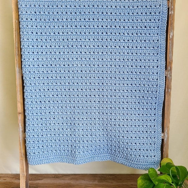 Image shows the crossed double crochet blanket in blue, folded in half and draped over a wooden blanket ladder. 