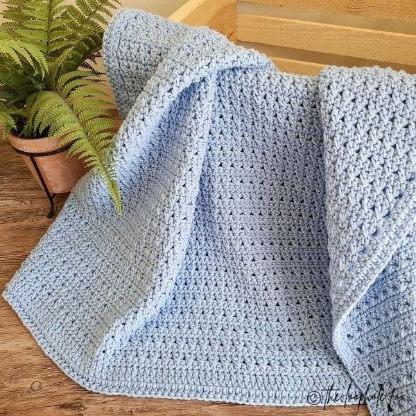 Image shows the crossed double crochet baby blanket draped over a wooden decorative crate. 