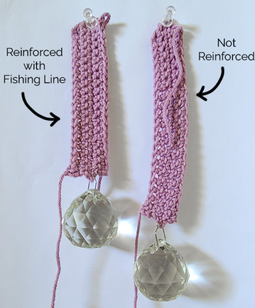 Picture showing the test done to conclude whether or not using fishing line helped keep the crochet strap non-stretchy. Long swatches create "mini straps" in a light purple yarn, and glass prisms are hung from the bottom as weights.