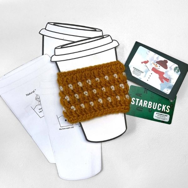 This image shows the Coffee Cozy designed by Revel. The coffee cozy is shown on a cardstock cup cutout, as it would be shown if you were purchasing it at a craft fair.