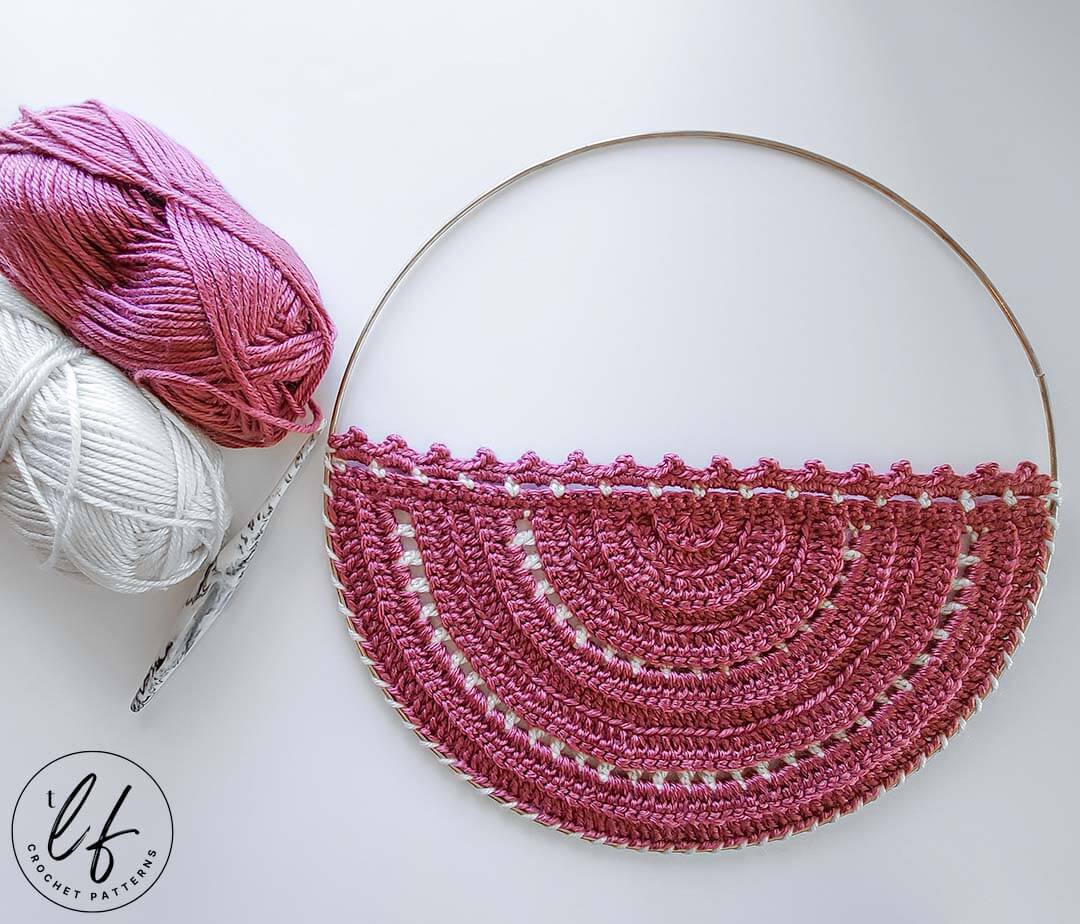 This image shows the crochet wall hanging free pattern sample laid flat on a white background. The two colors of yarn used sit at the top left hand corner with a crochet hook. 
