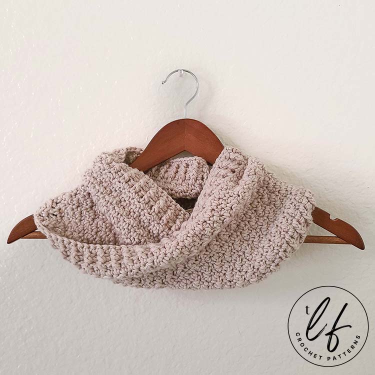 The crochet infinity cowl pattern is shown finished, hanging on a wooden hanger with a white background.