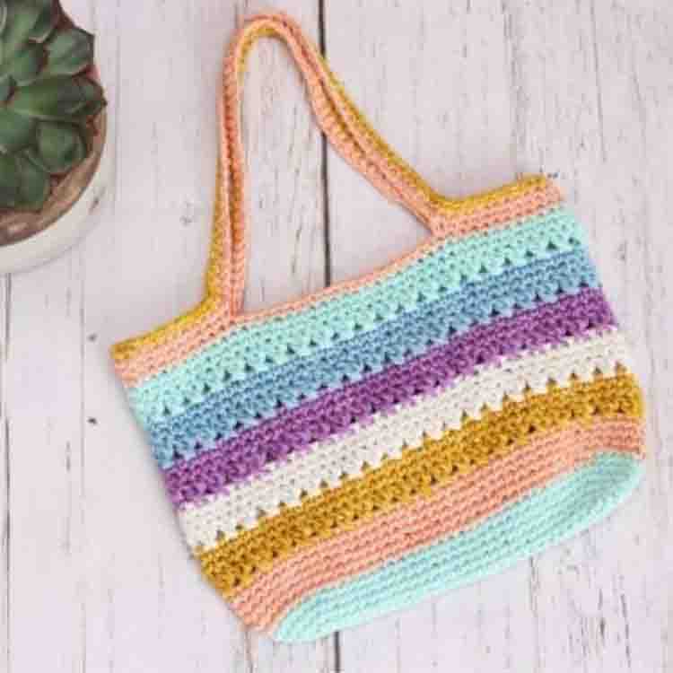 This image is of the Criss Cross Mini Tote, one of the crochet projects for spring. This image shows the bag laying flat on a wooden background.