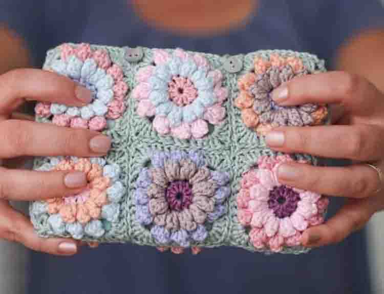 This image is of the Flower Clutch, one of the crochet projects for spring. This image shows a woman holding the clutch in front of the camera. Only the clutch and her hands are visible in the picture.