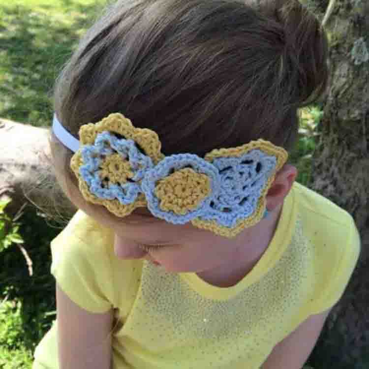 This image shows a little girl wearing the Bloom Headband. The little girl is looking down so you can see the pretty flowers on the headband.