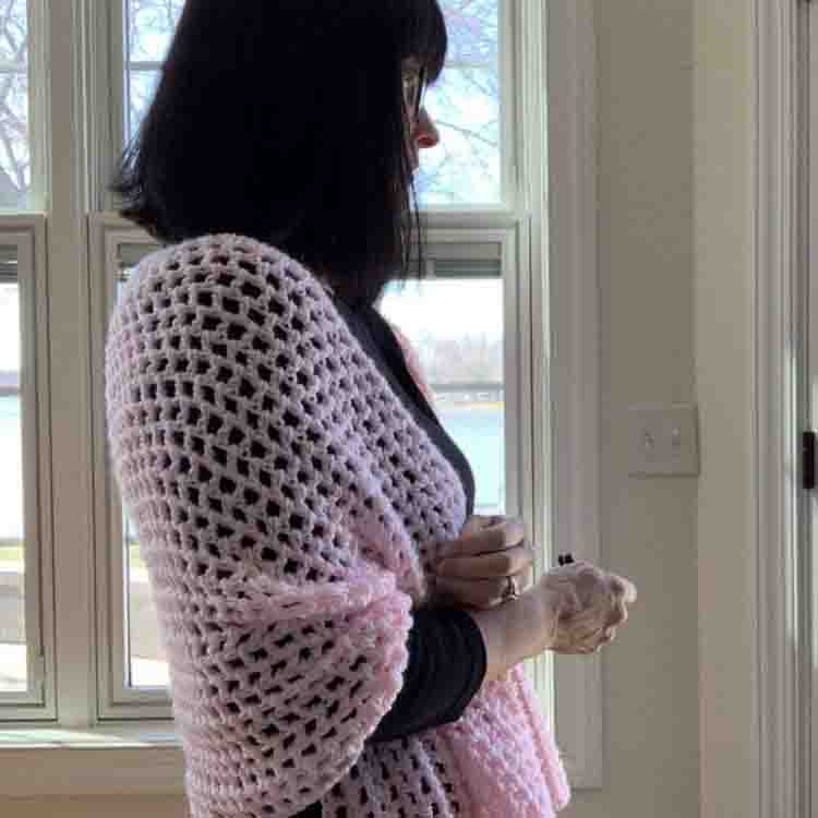 This image shows a woman standing in front of a window, wearing the Touch of Spring Shawl.