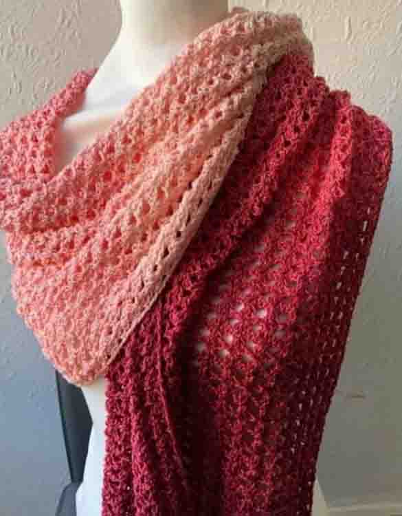 This image is of the Shanae Shawl. The shawl is wrapped on a white mannequin in front of a white wall. The shawl is made in deep reds and pinks. 