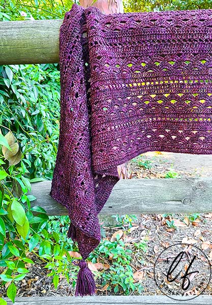 This image shows the crochet rectangle shawl pattern sample laying draped on a wooden fence with trees and bushes in the background.