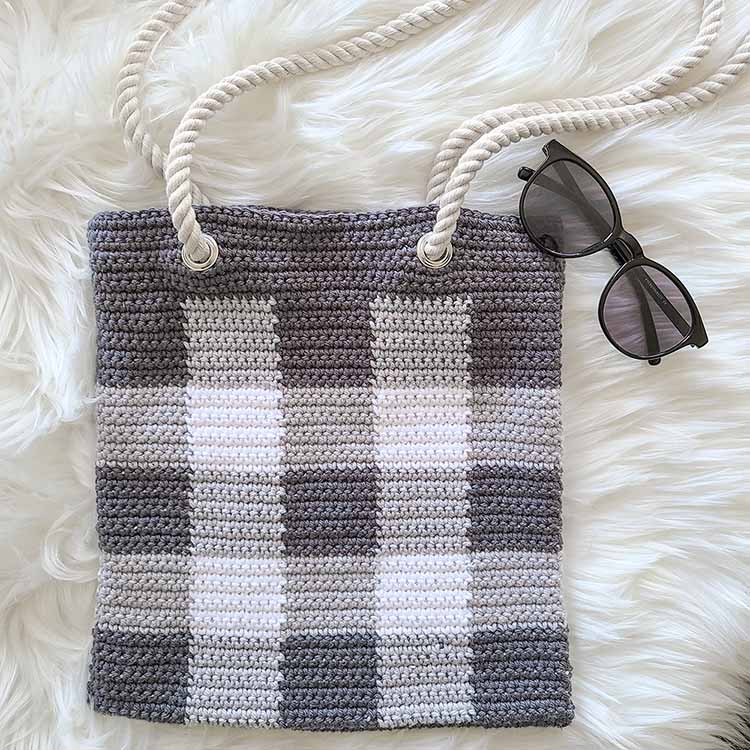This image shows the crochet gingham tote bag laying flat on a fluffy white surface.