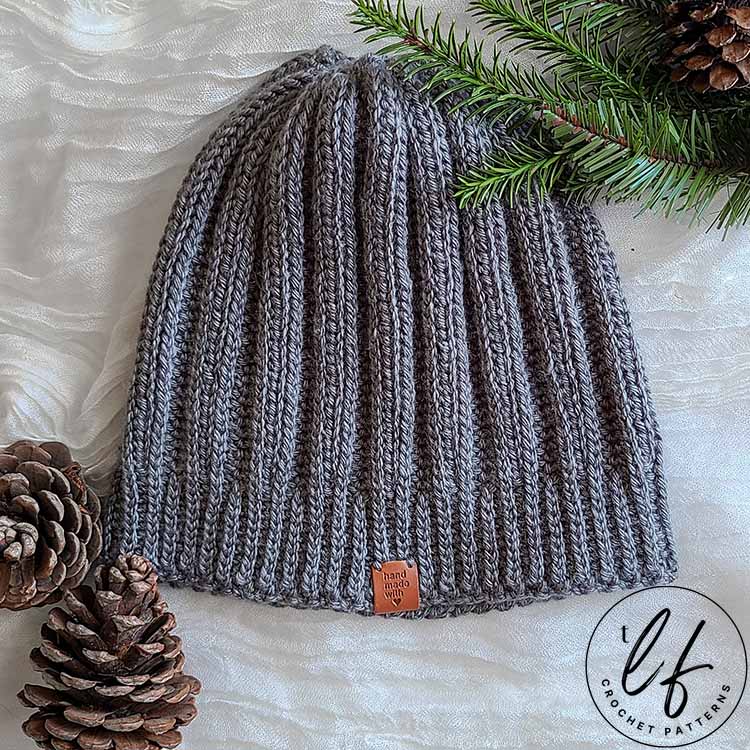 This image shows the ribbed crochet beanie pattern in medium (4) weight, Lion Brand Homeland in Petrified Forest. This is a greyish green color. The beanie is sleek with many more ribs than it's super bulky version.