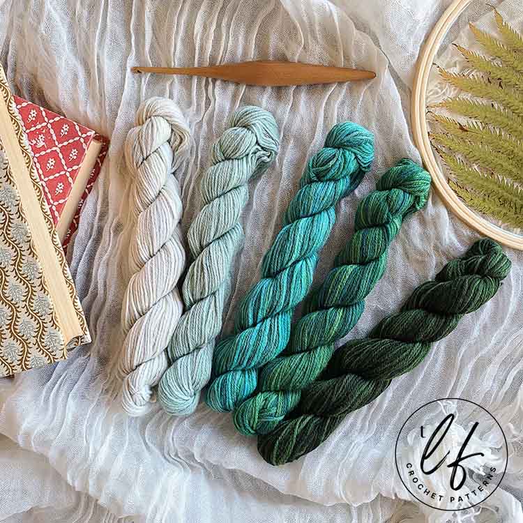 This image shows all 5 mini hanks that came with the Stroll Tonal Mini Pack from We Crochet. They are arranged lightest (left) to darkest (right) and are laying on a fabric surface.