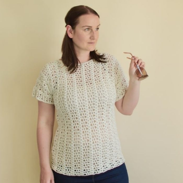 This image shows the Summer Romance Top, one of the crochet projects for summer, worn by a woman in front of a taupe background.