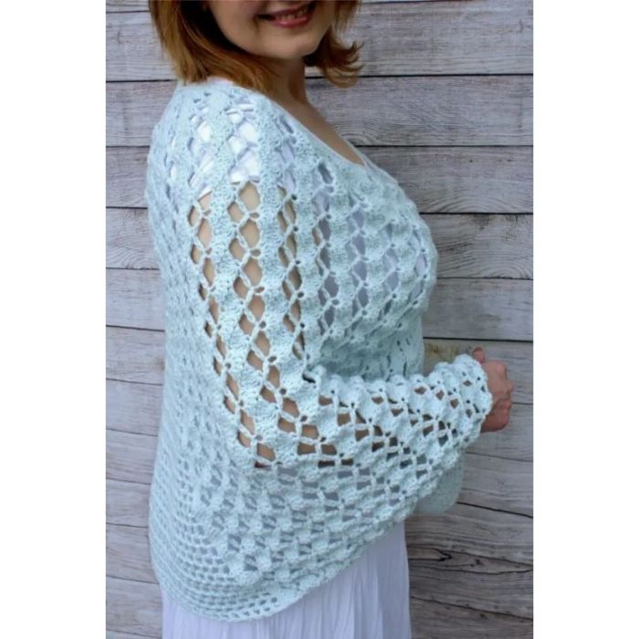 This image shows the Whimsical Waves Poncho, one of the crochet projects for summer, worn by a woman who is standing to show the side. She is standing in front of a wooden wall.