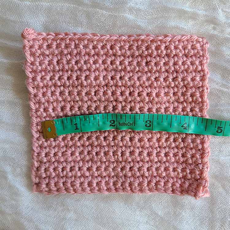This image shows a swatch of single crochet stitches with a cloth measuring tape set across it horizontally, or parallel to the stitches. This is demonstrating how to measure your crochet gauge for stitches.