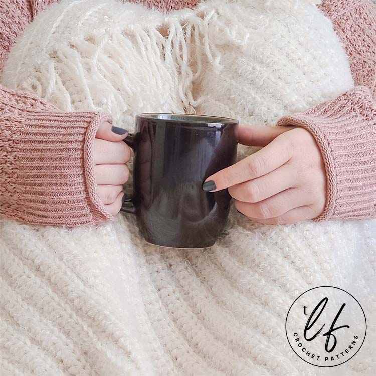 This image is a close up of the half double crochet blanket pattern sample. A woman has the blanket draped over her knees and she is holding a coffee cup. You can see the details of the ribbing in the blanket.