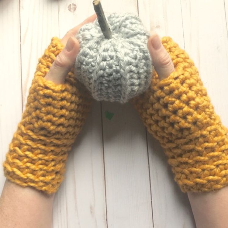 This image shows the next pattern, which is the Oh So Cozy Fingerless Gloves as described above. The image shows the gloves being worn and the hands holding a crocheted pumpkin. 
