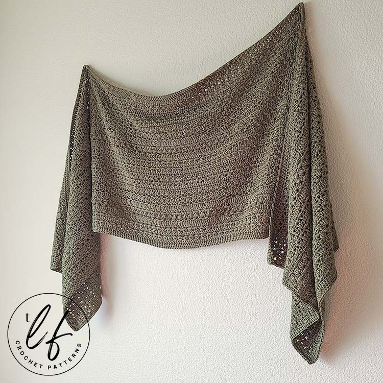 This image shows the crochet wrap pattern finished and hanging on a white wall. It is pinned lengthwise and shows the drape of the finished work.