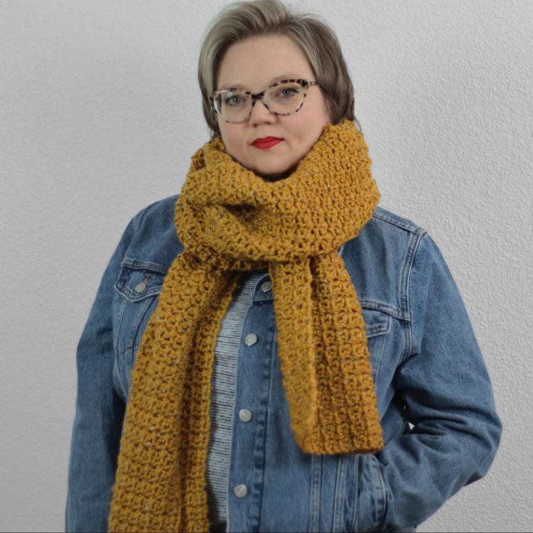 This image shows the next pattern, which is the Pecci scarf as described above. The image shows the scarf worn by a woman who is standing in front of a white background.