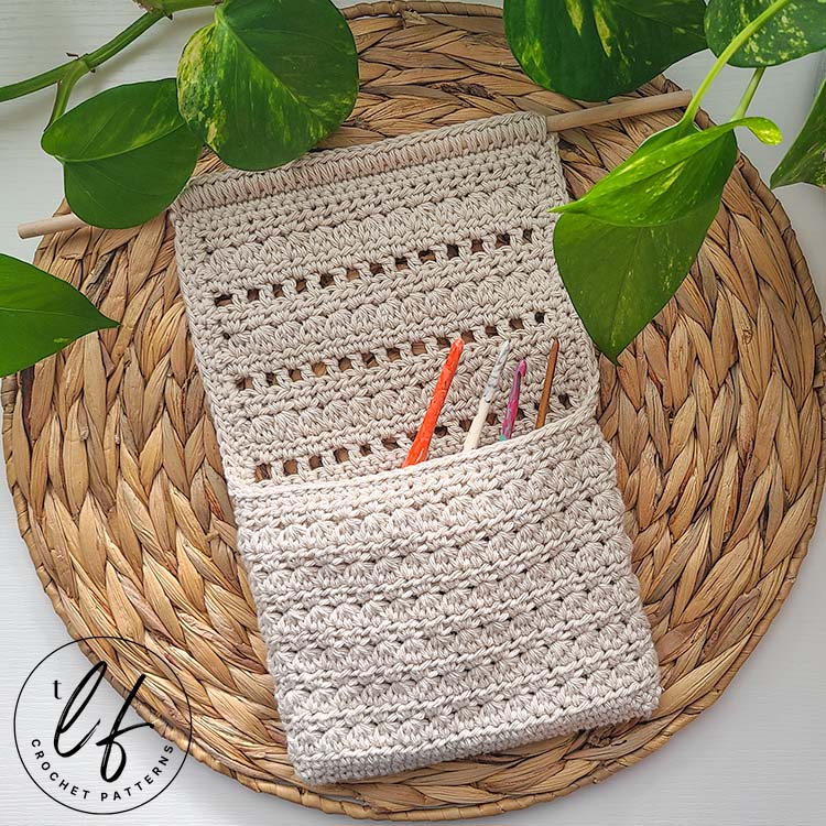 This image shows 1 finished basket created from this Crochet Hanging Basket Pattern. The basket is laying flat on a woven, natural placemat with a strand of pothos laying at the top. In the basket are crochet hooks.