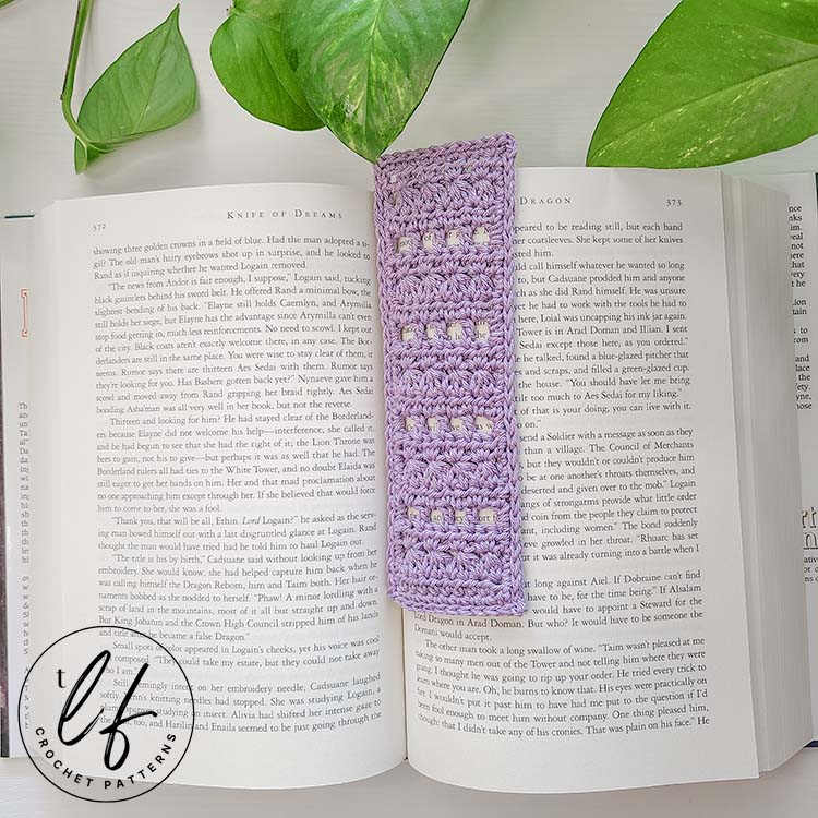 This image shows the finished project made from this Lace Crochet Bookmark Pattern in an open, hardback book that is large sized. The bookmark is made in a lavender color.