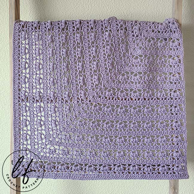 This image shows a finished sample of the flower square crochet pattern. The pattern has been worked in lavender yarn and is shown draped over a blanket ladder.